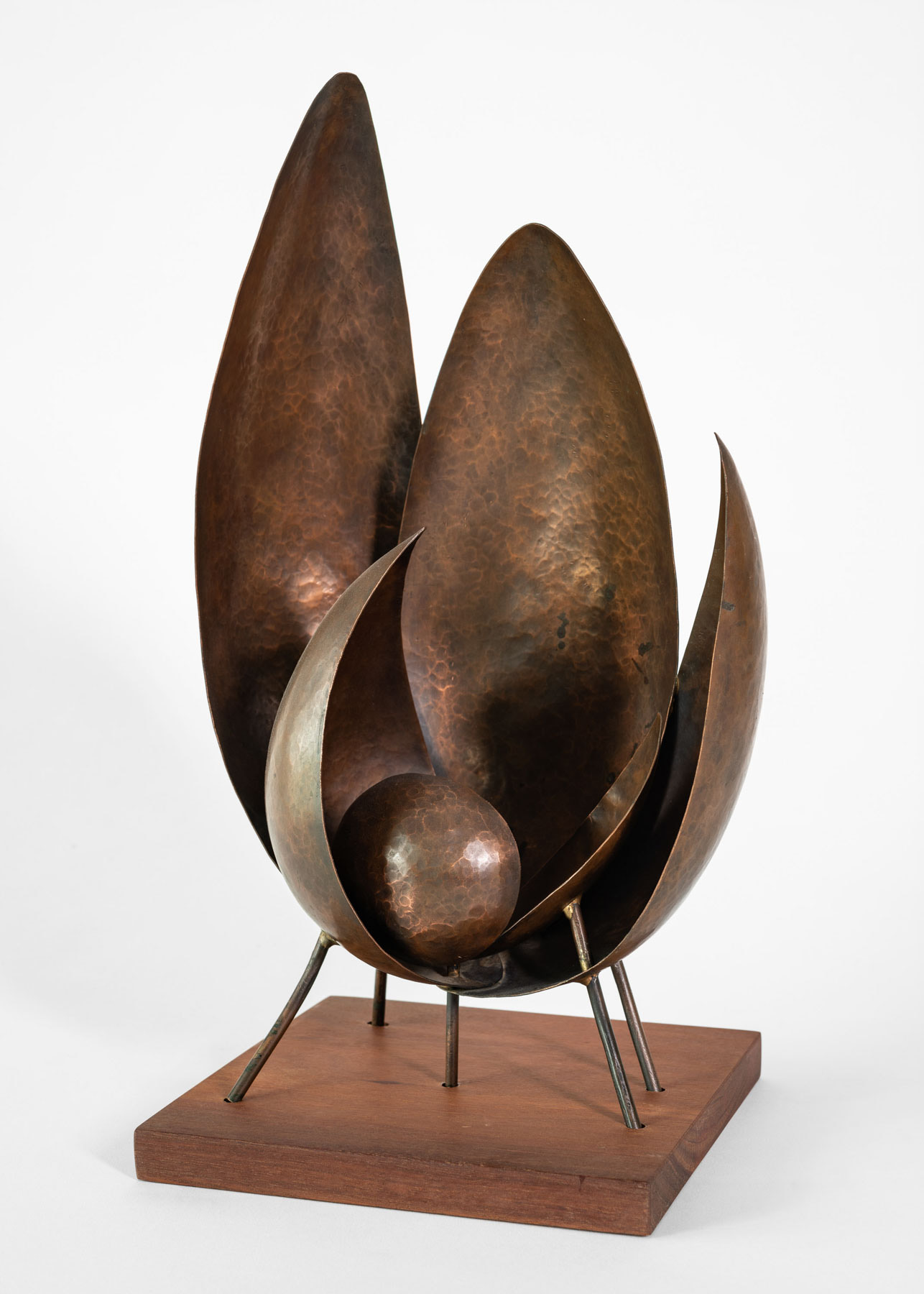 A bronze sculpture with leaf-like shapes reaching upward and a sphere cradled at the bottom of the flat, broad leaves.