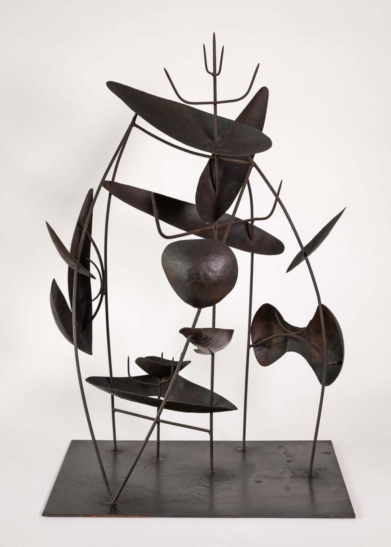 A metal sculpture with long, skinny spikes bent in different directions with organic shapes attached in various spots.