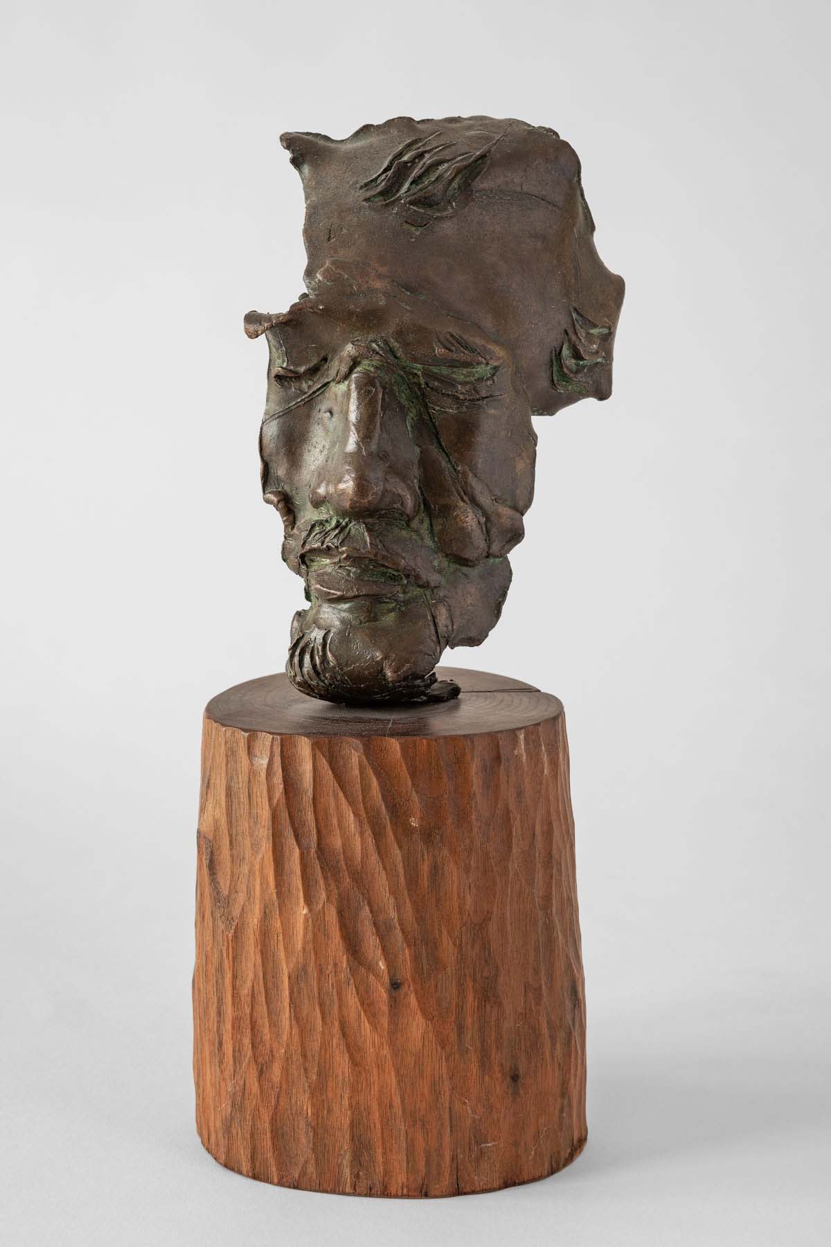 Partial bronze bust of a man with closed eyes mounted on a wood pedestal.