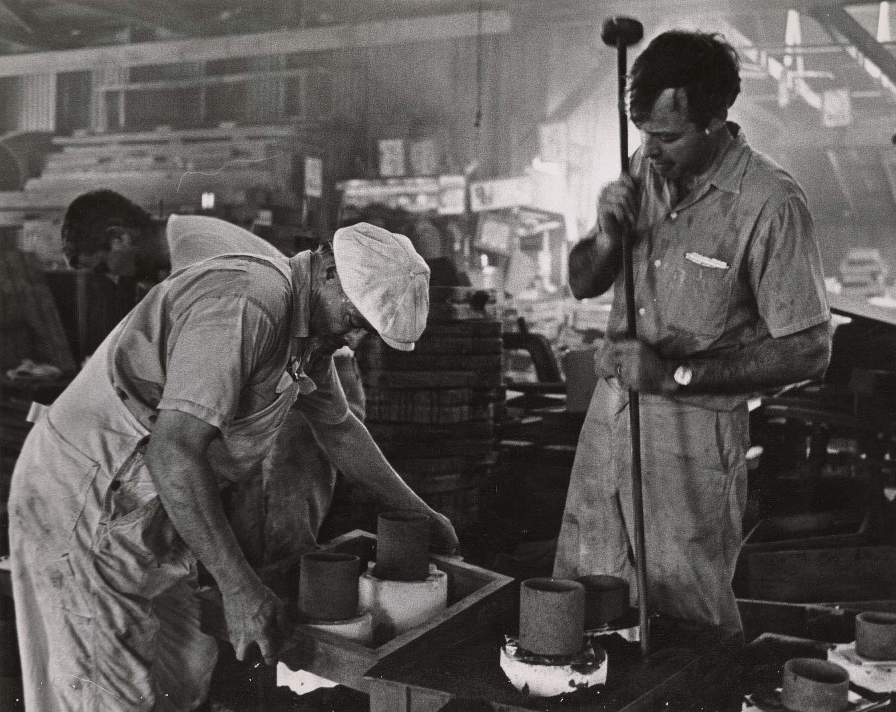 A black-and-white photograph of two men working on a project in a steel foundry.
