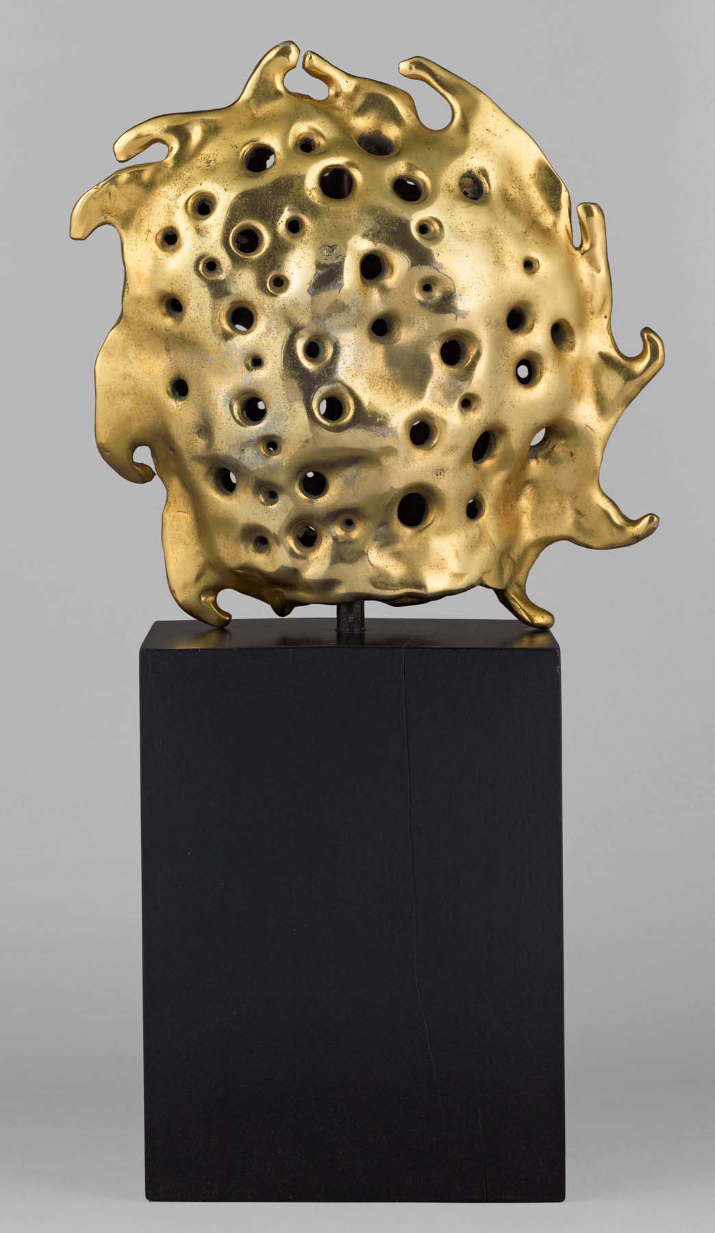 A bronze sculpture of a gold sun sitting atop a tall, dark rectagular base.