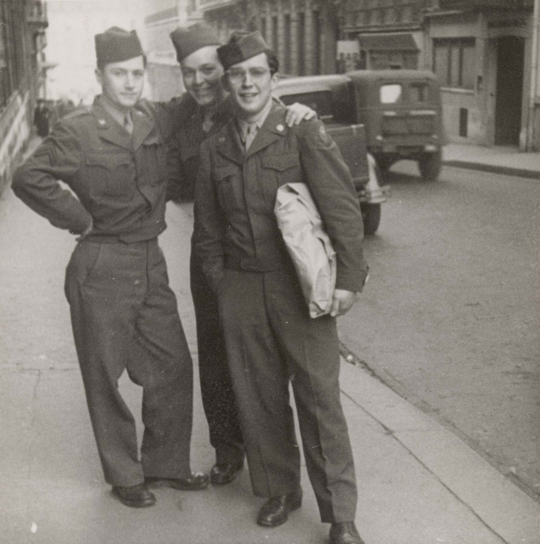 A black-and-white photograph of three male soldiers standing together on a city street.