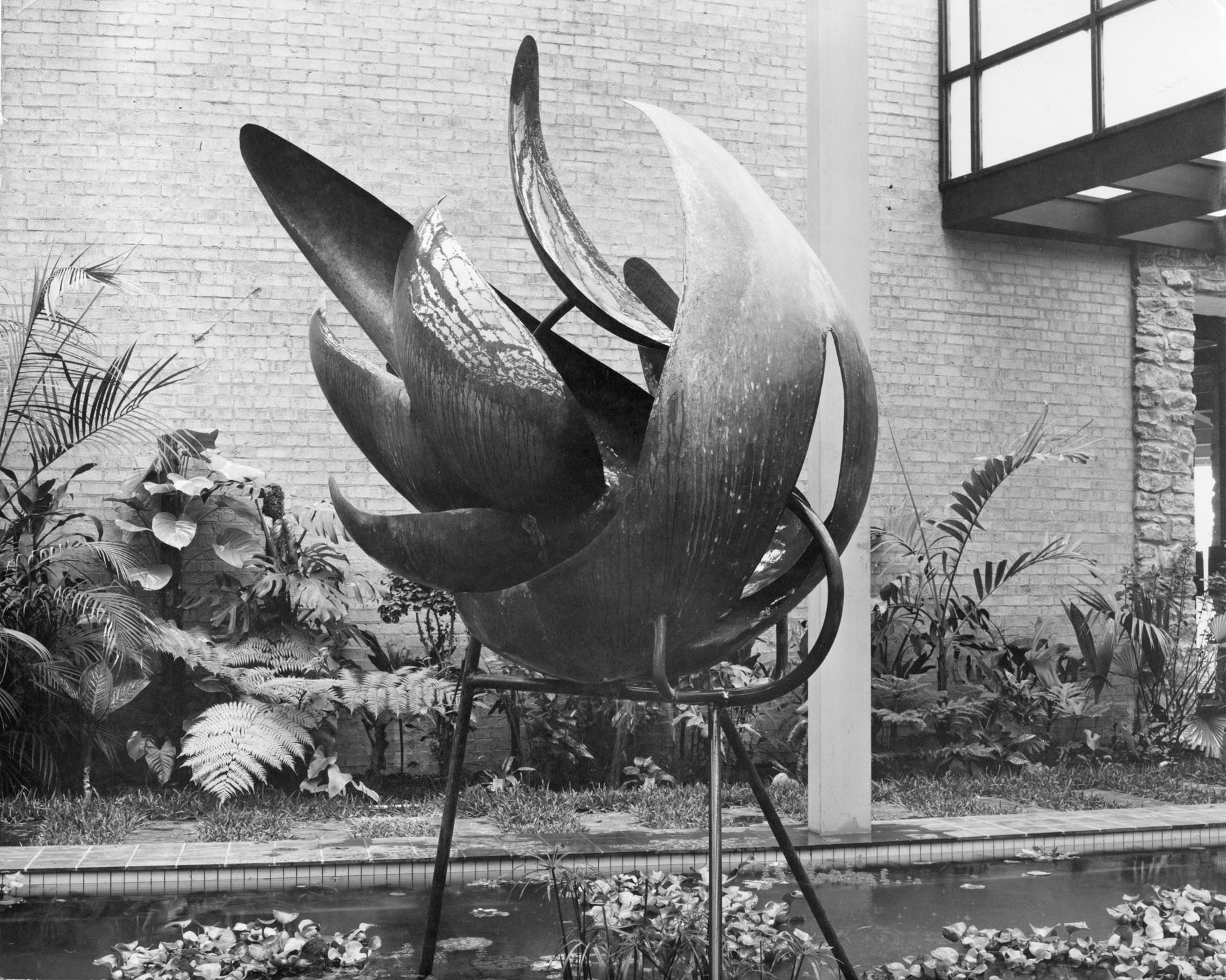Black-and-white photo of a flower-like sculpture situated within landscaping.