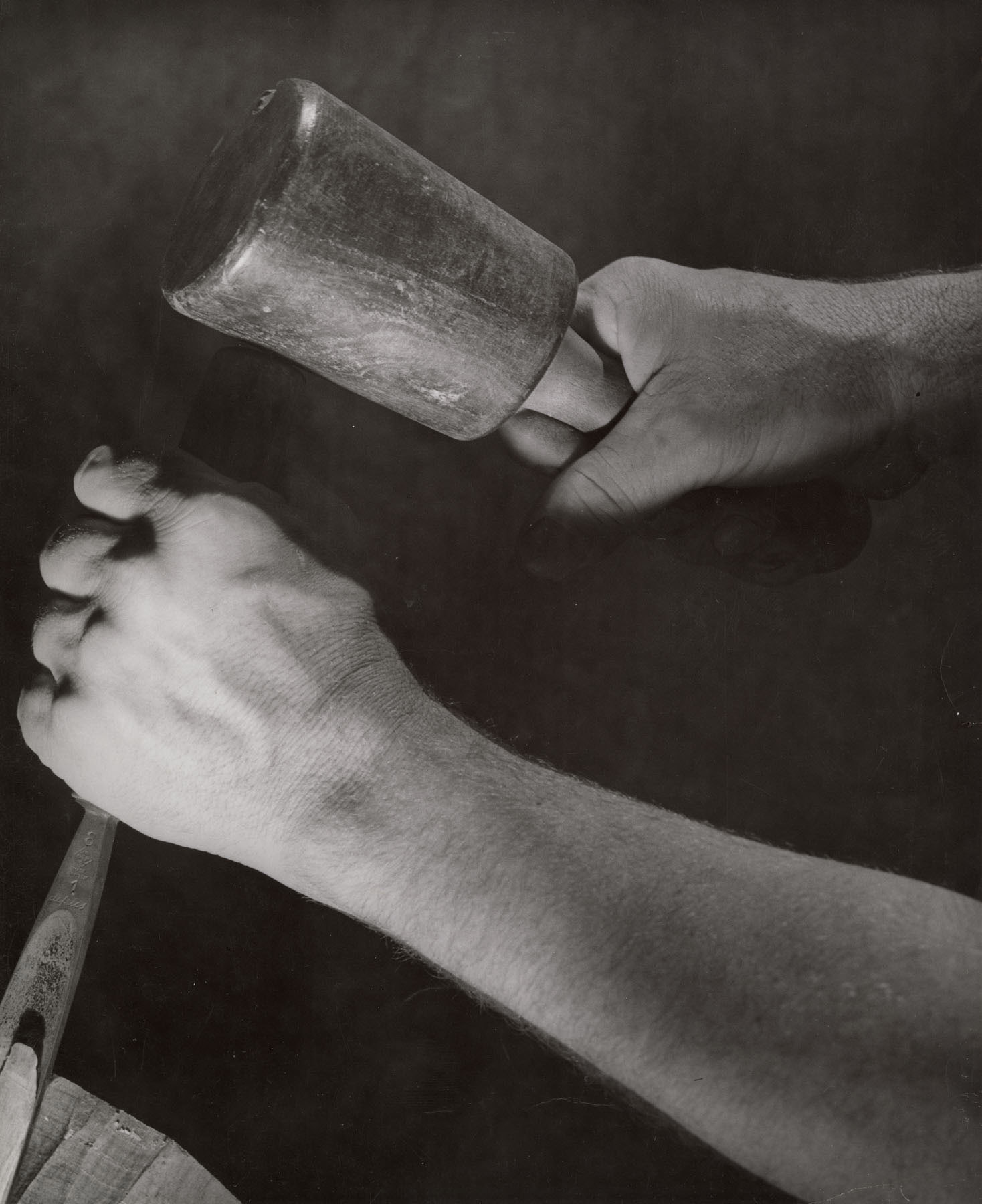Black-and-white photo of hands holding a chisel in one and a mallet in the other.