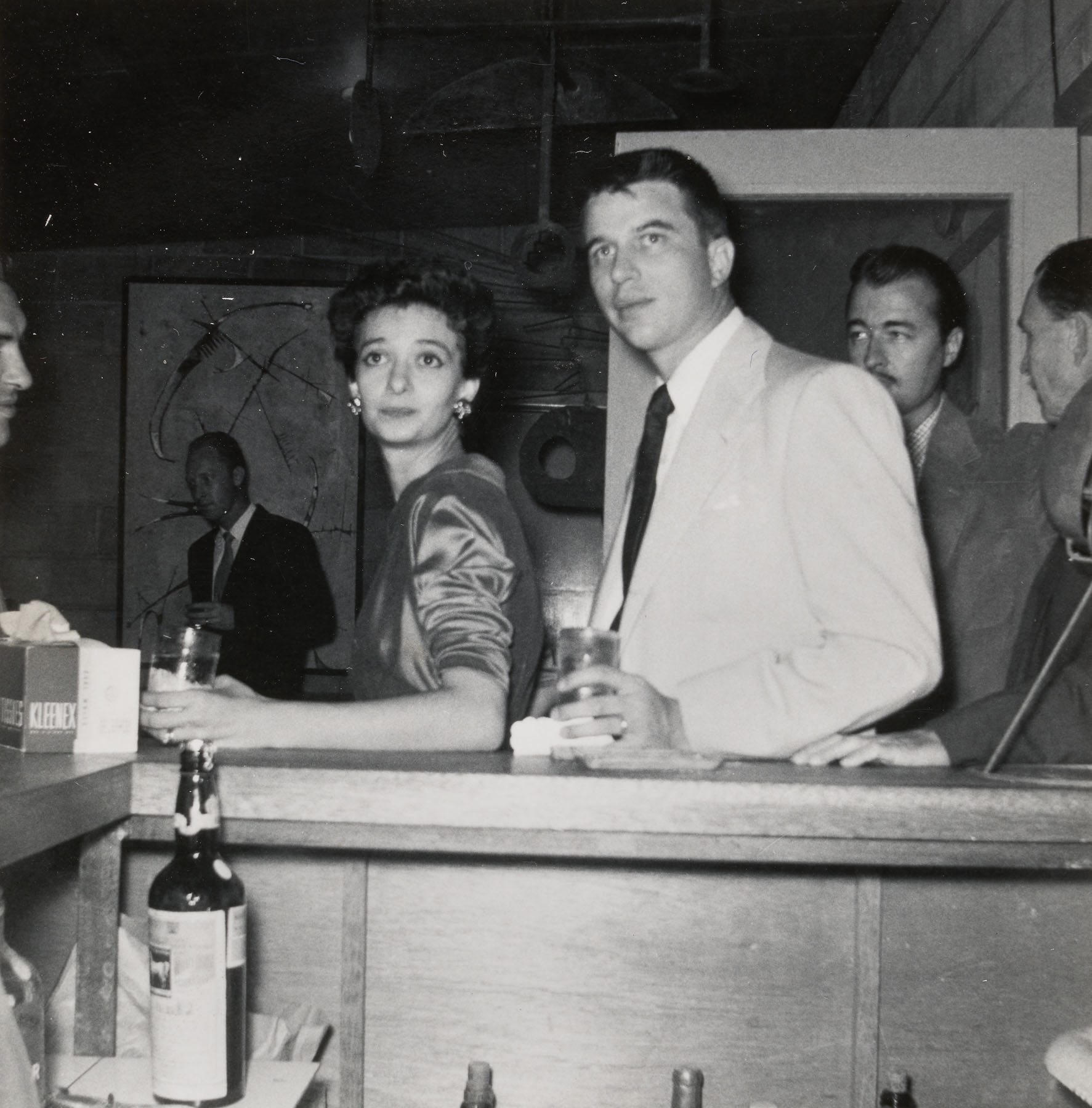 Black-and-white photo of a woman and a man at a bar holding drinks in their hands.