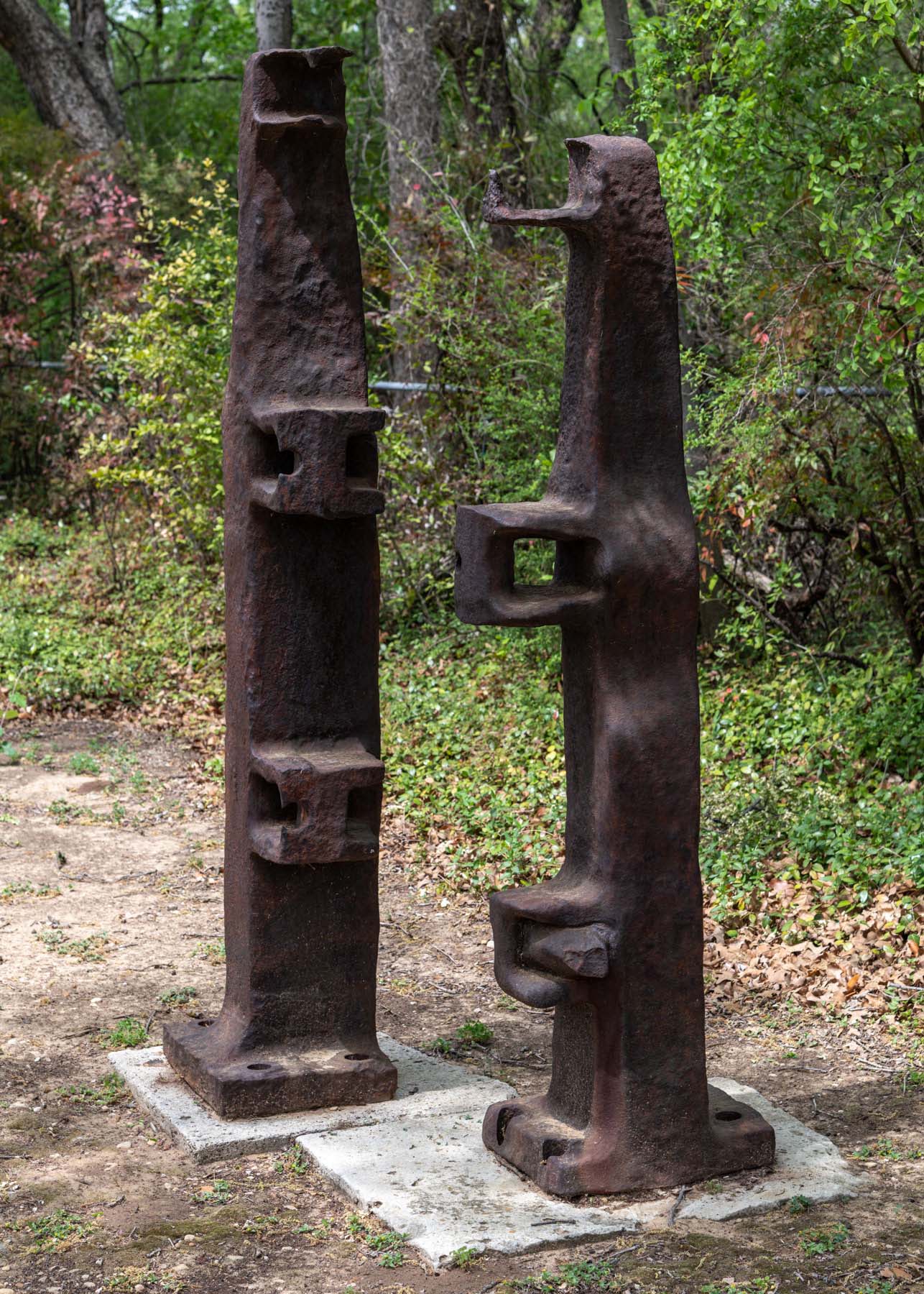 Two tall, rusty, industrial-looking totems with rectangular protrusions stand next to each other outdoors.