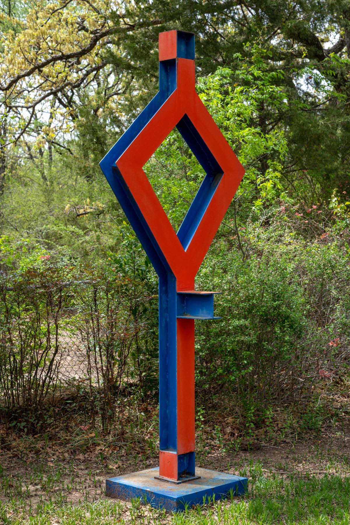 Red and blue outdoor sculpture made of steel beams with a diamond shape in the middle.