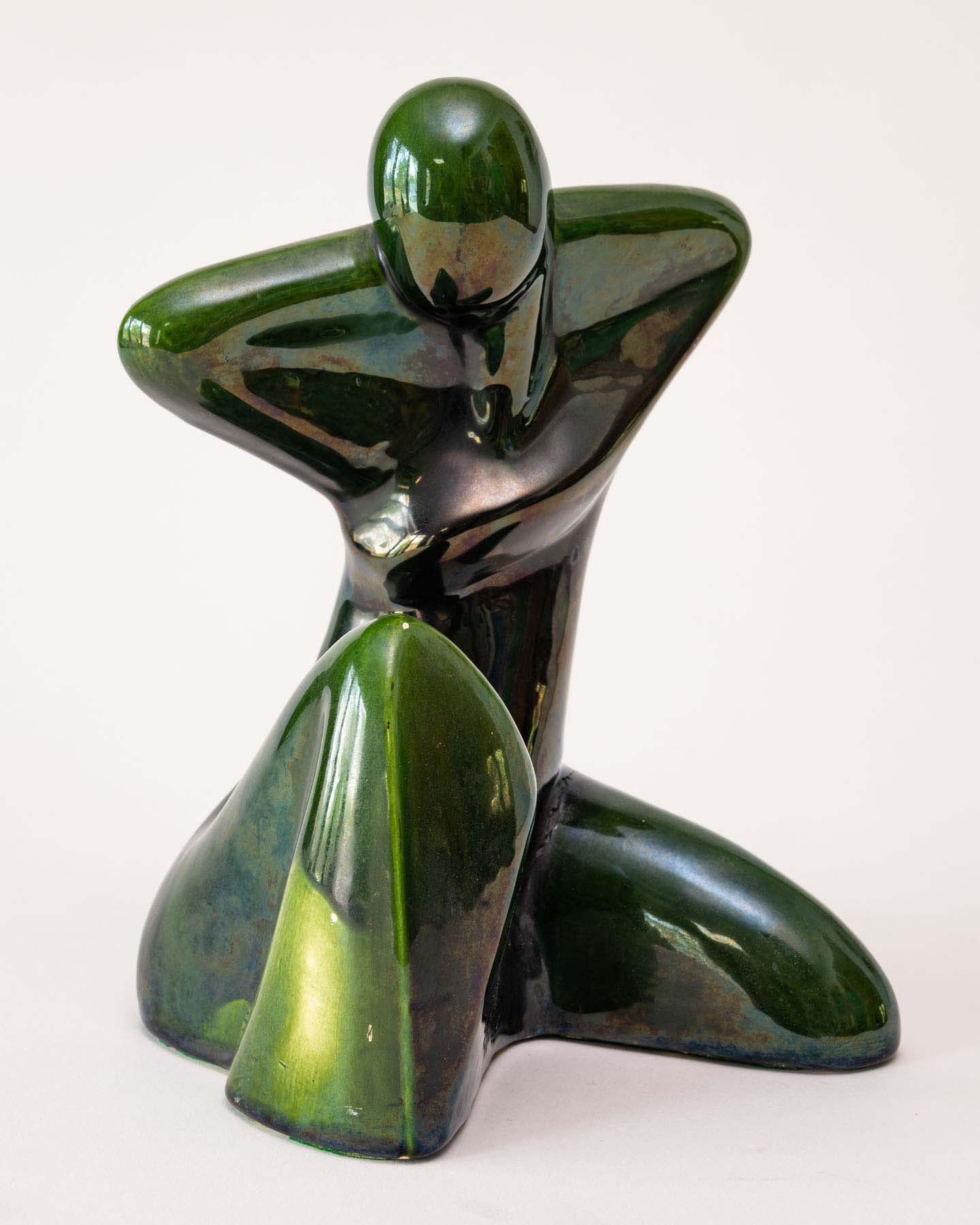 A smooth, ceramic abstract sculpture of a person sitting with one knee bent upwards and their arms behind their head.