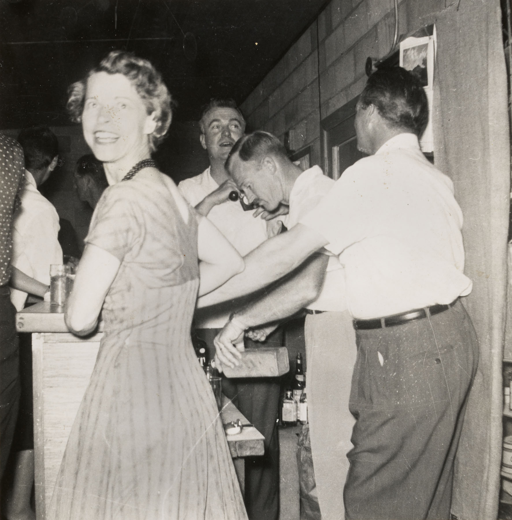 Black-and-white photo of a group of people standing around a bar.